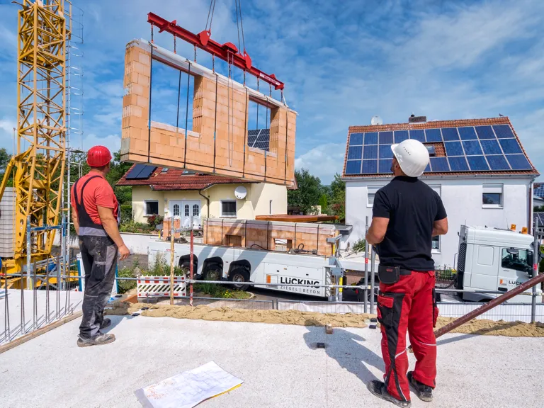 Foto: Ziegel-Element-Fertigwand wird von zwei Bauarbeitern mit Kran gesetzt.