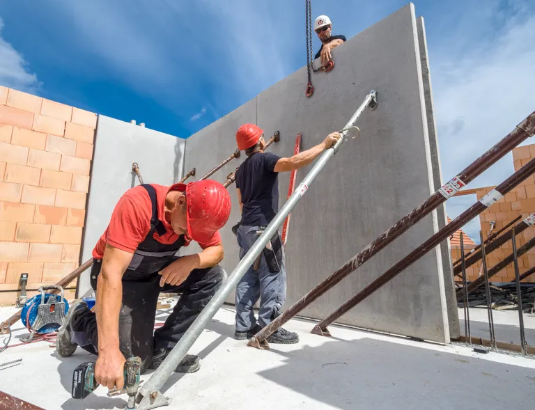 Foto: Beton-Element-Doppelwand wird von zwei Bauarbeitern fixiert.