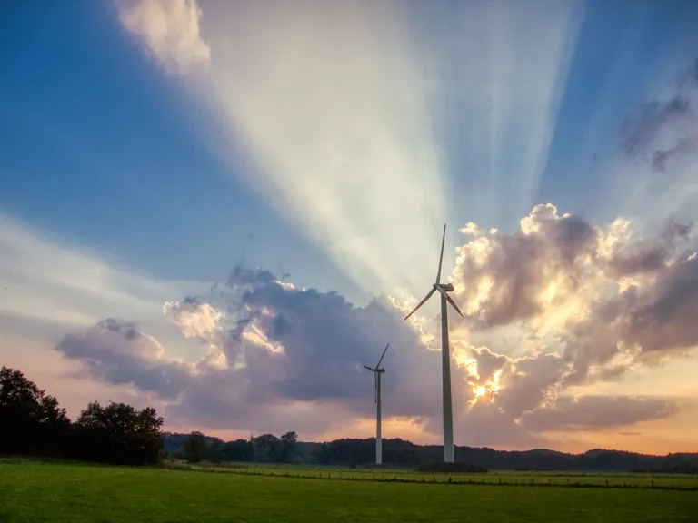 Foto: zwei Windkraftanlagen auf Feld im Abendlicht