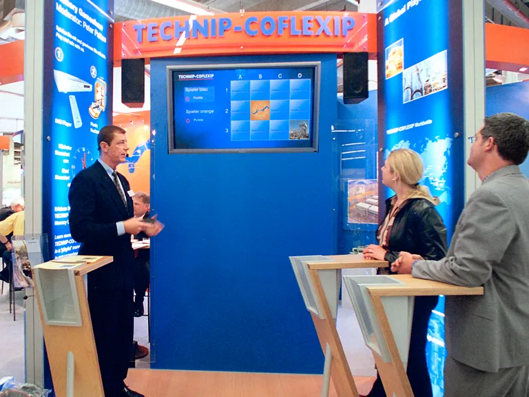 Moderator und drei Messebesucher vor Monitor mit Memory-Game-Show