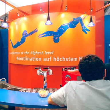 Foto: Grafische Umsetzung des Messemottos: „Koordination auf höchstem Niveau“ mit Trapez-Artisten als Bildmetapher am Meeting-Point